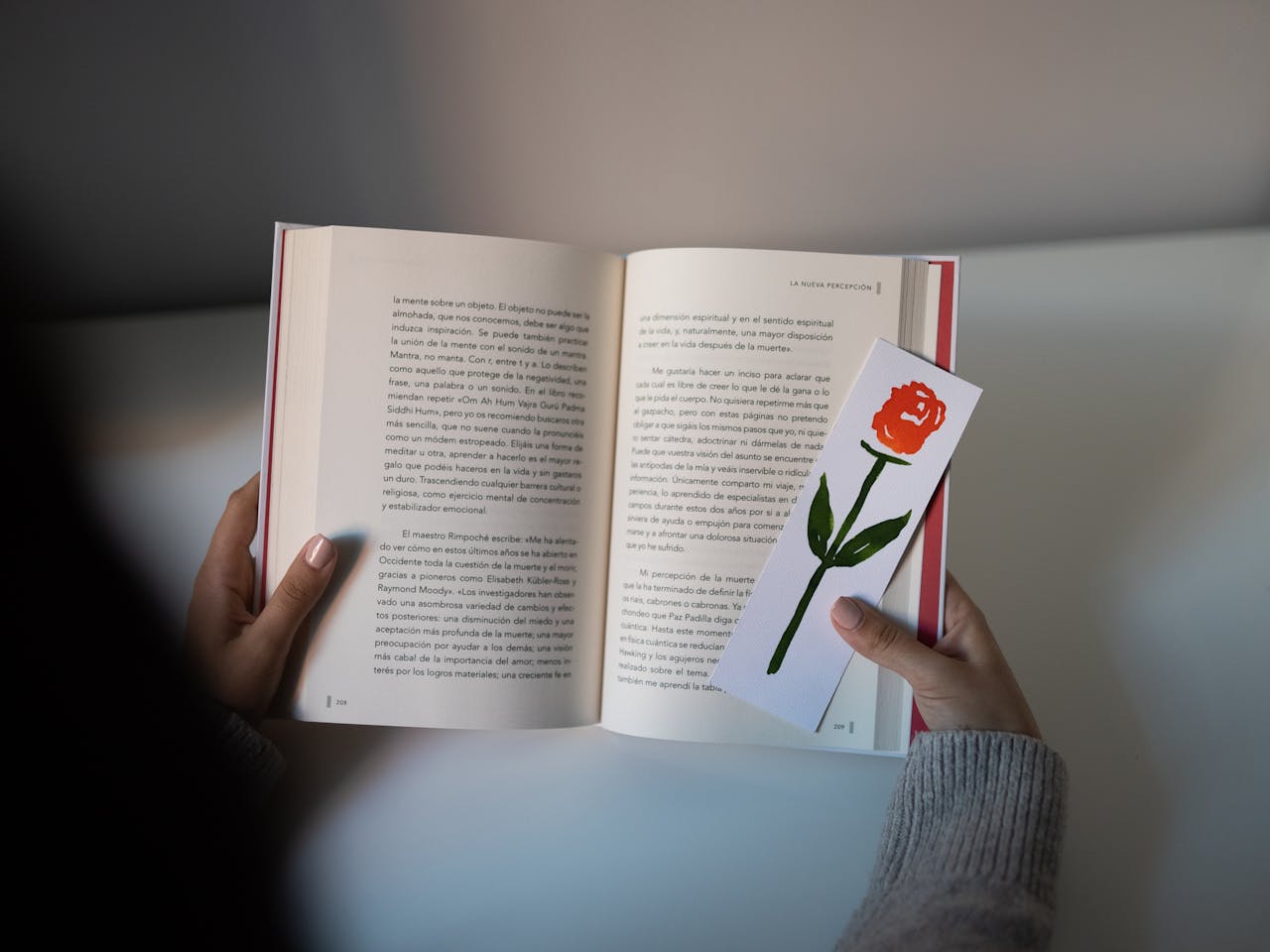 A person holding an open book with a floral bookmark, depicting reading and relaxation.