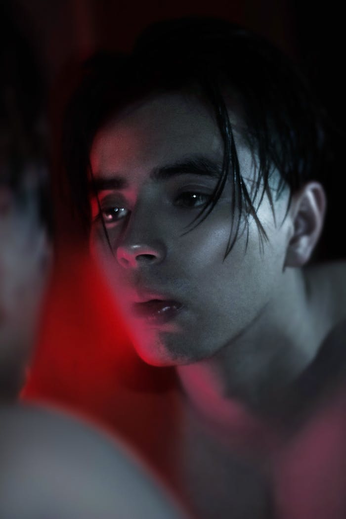 A reflective portrait of a man looking at his mirror image amidst a dark, moody setting.